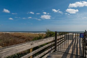 Ein hölzerner Steg führt zu einem Strand unter blauem Himmel.