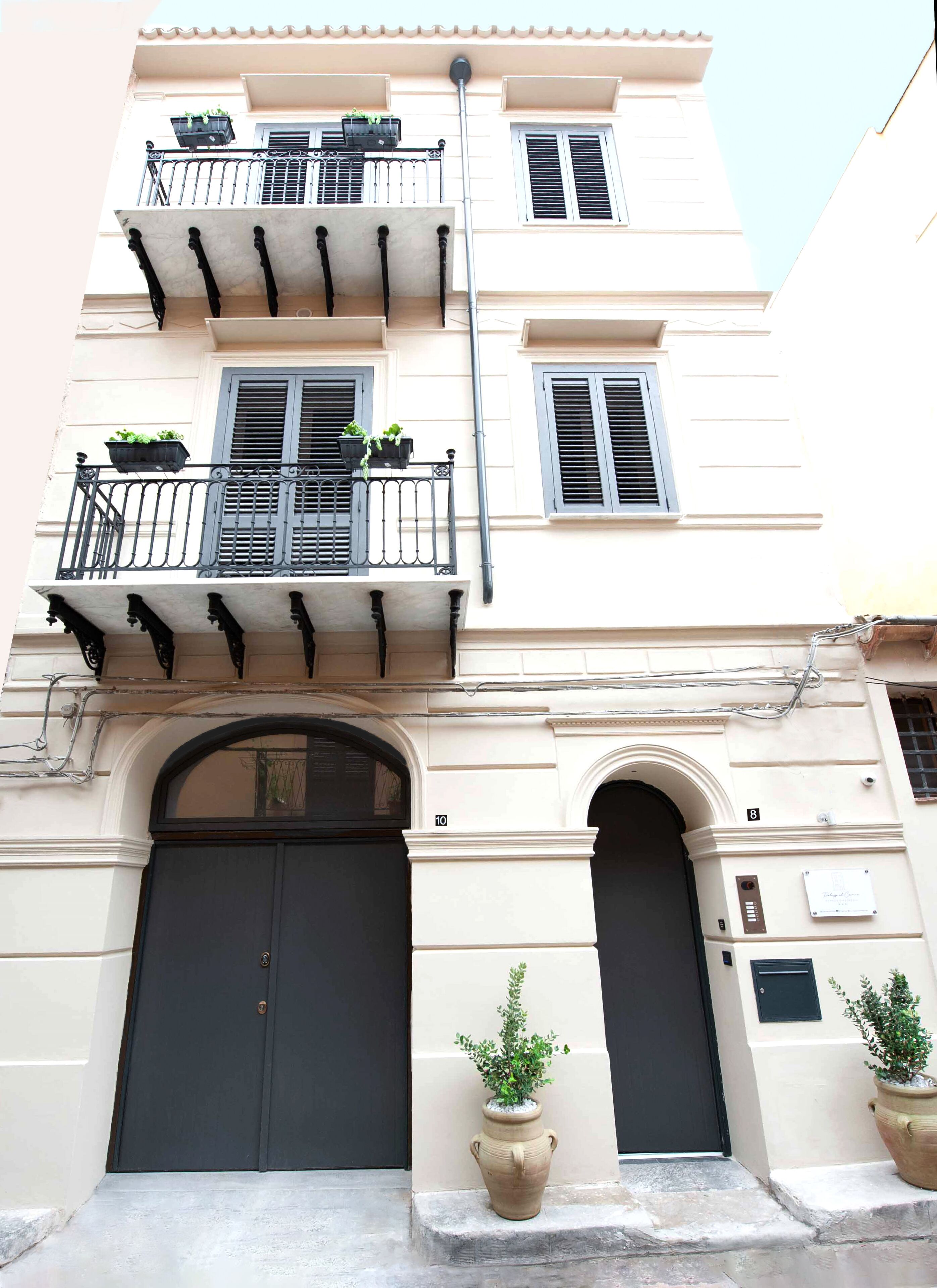 A building with a large central door, two balconies with black railings, and potted plants on the ground floor.