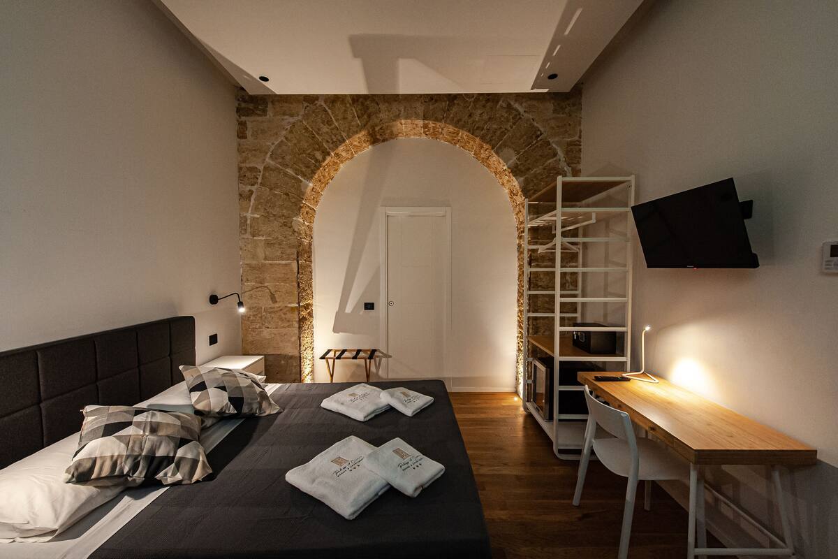 Een moderne slaapkamer met een stenen boog, een bed met handdoeken, een bureau met lamp en een aan de muur bevestigde televisie.