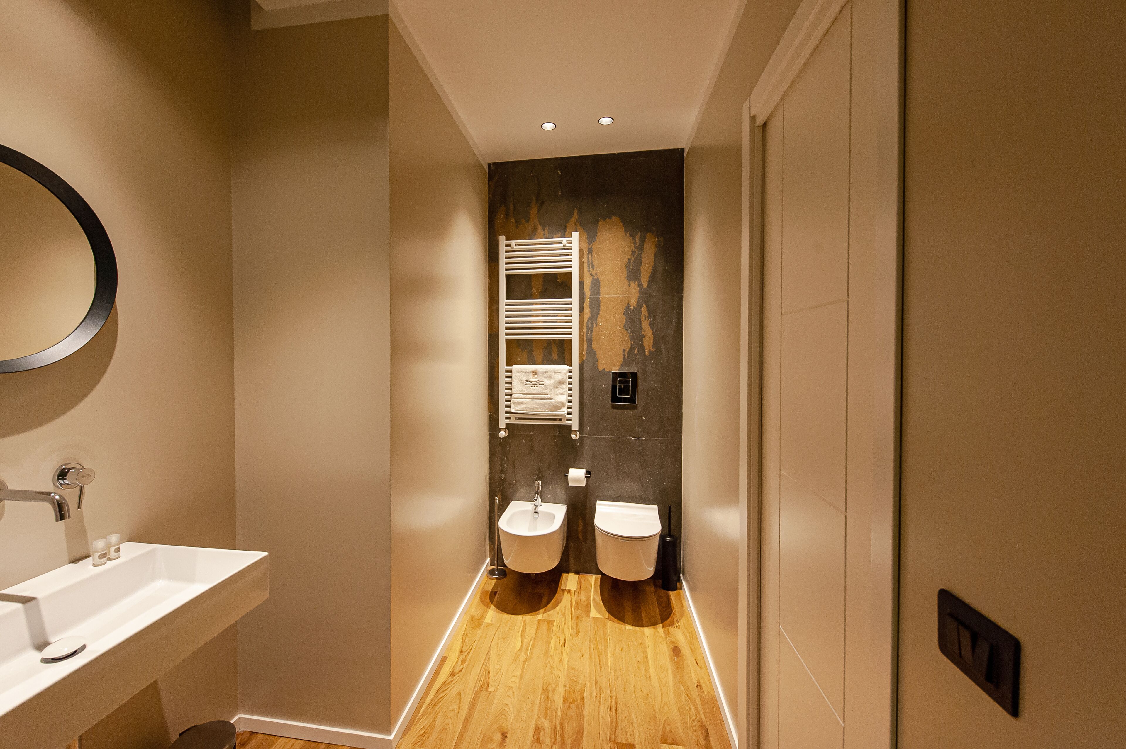Een moderne badkamer met een houten vloer, twee wastafels, een handdoekhouder en een spiegel.