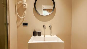 Un bagno con un lavandino bianco, uno specchio rotondo e un asciugacapelli fissato alla parete.