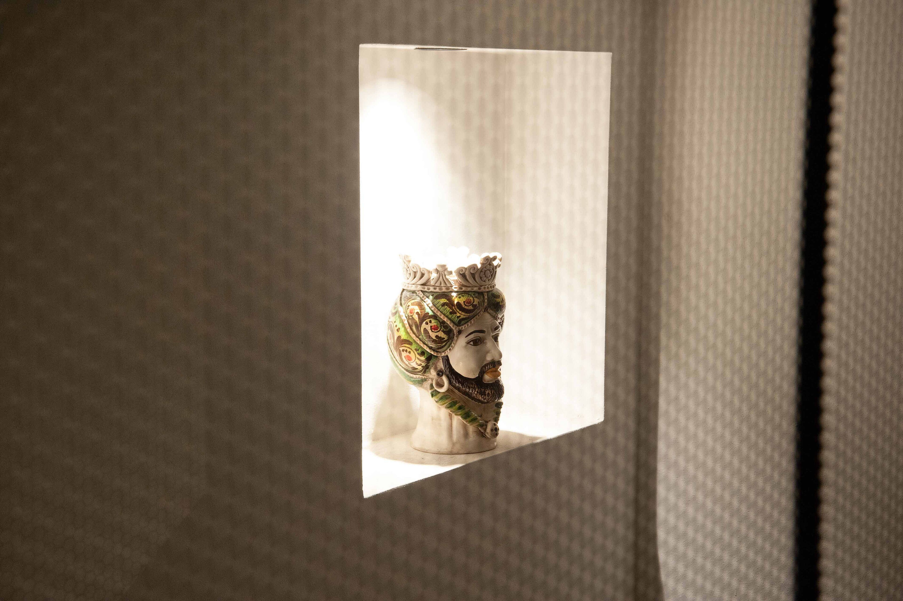 Een gebeeldhouwd borstbeeld in een lijst van een historische persoon met een kroon, tentoongesteld tegen een structuurrijke muur.