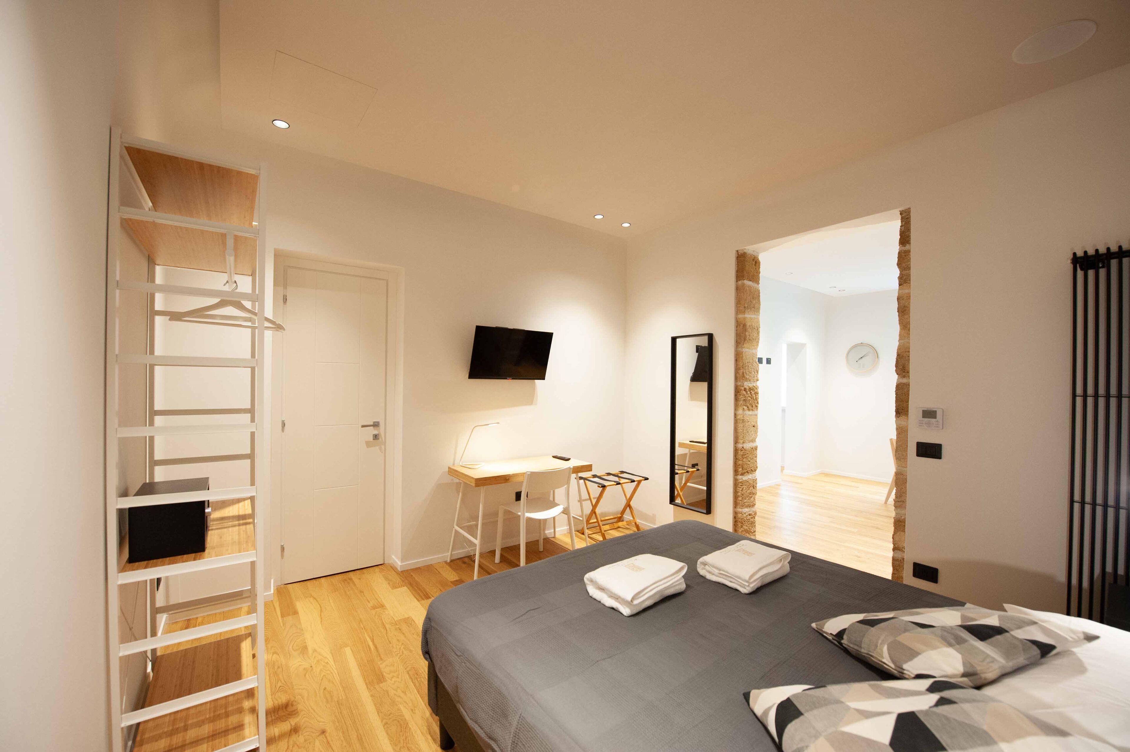 Una camera da letto moderna con un letto, una scrivania, una sedia, una TV e un armadio.