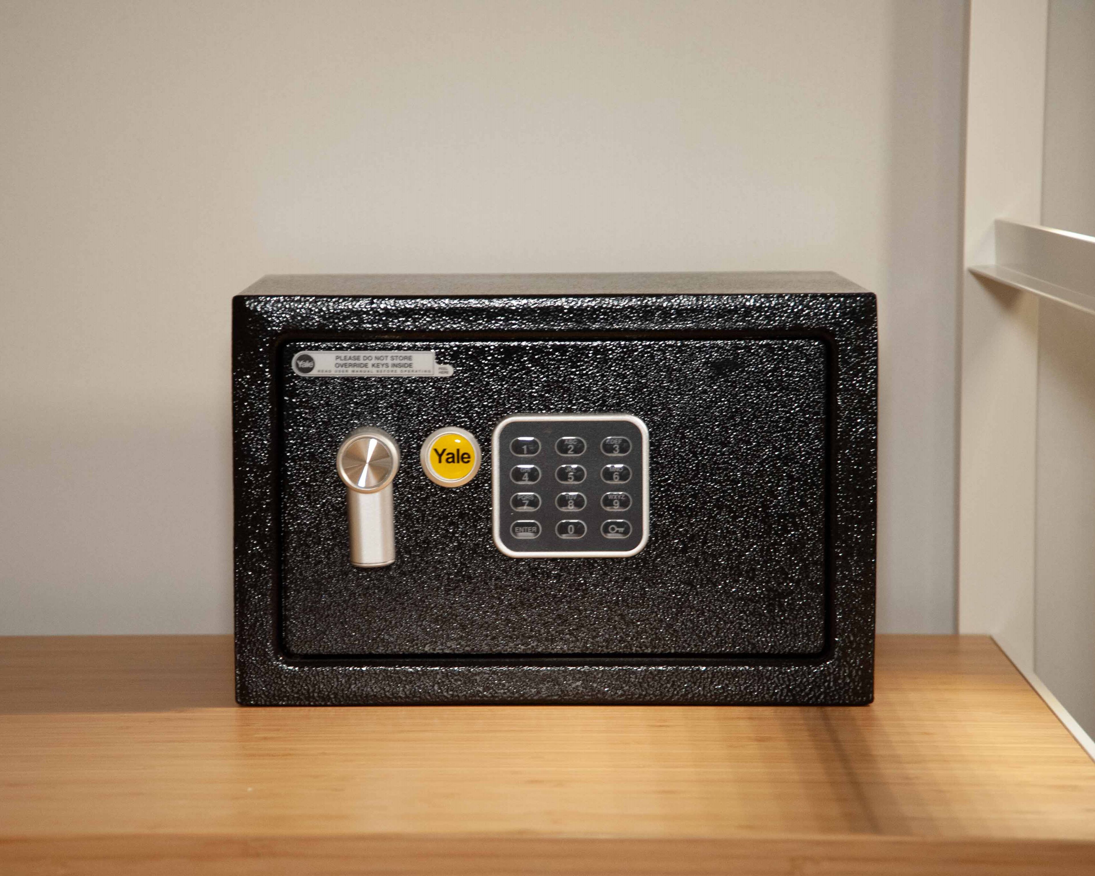 A black safe with a Yale lock and keypad on a wooden surface.