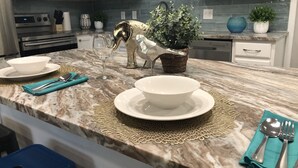 Una cocina con armarios blancos, encimera de mármol, un adorno dorado y una planta en maceta.