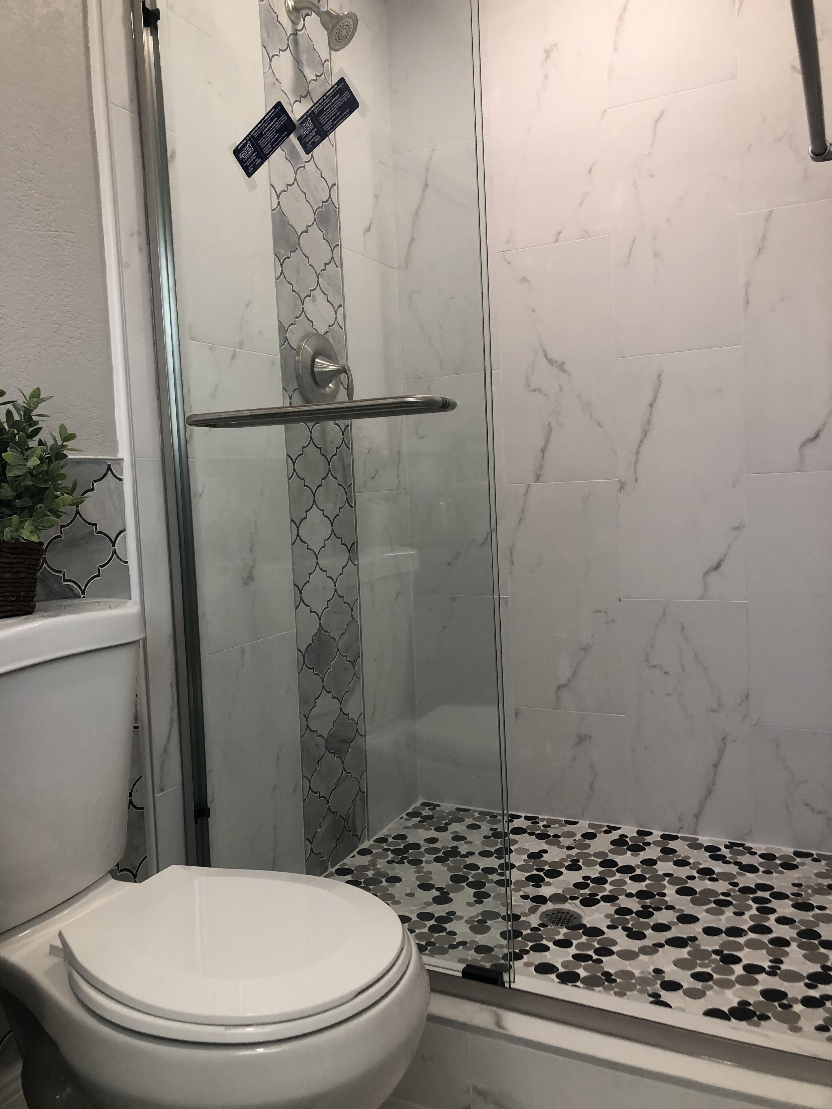 A bathroom with a glass shower enclosure, a toilet, and a patterned floor.