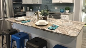 Una cocina moderna con armarios blancos, electrodomésticos de acero inoxidable y encimera de mármol. Hay tres taburetes y un lavamanos con grifo.