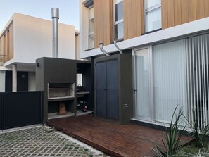 Een modern gebouw met een grote schuifglazen deur, een houten terras en een metalen schoorsteen.