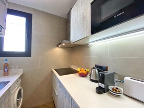 Compact kitchen with Bosch microwave, kettle, coffee maker, and toaster. Equipped with washing machine and sink.