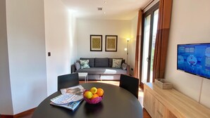 Ein modernes Wohnzimmer mit einer Couch, einem Fernseher und einem Esstisch mit einer Schüssel Obst.