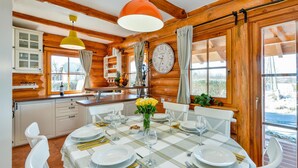 A wooden cabin interior with a dining table set for four, a clock, and a window with curtains. - Cozy home in Vinogradi Ludbreski with sauna (Vinogradi Ludbreski)