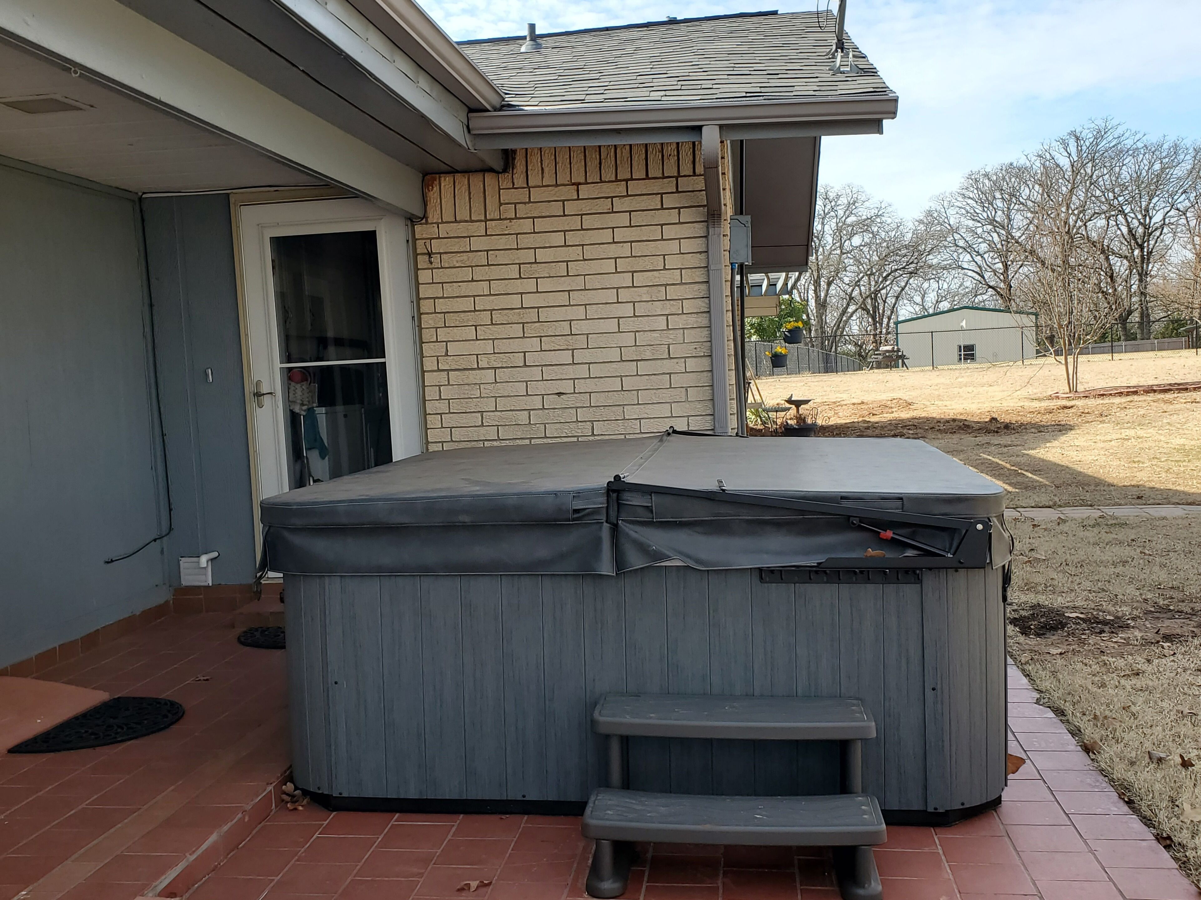Un jacuzzi extérieur abrité, doté d’un marchepied, d’un mur en briques et d’une porte donnant sur un garage.