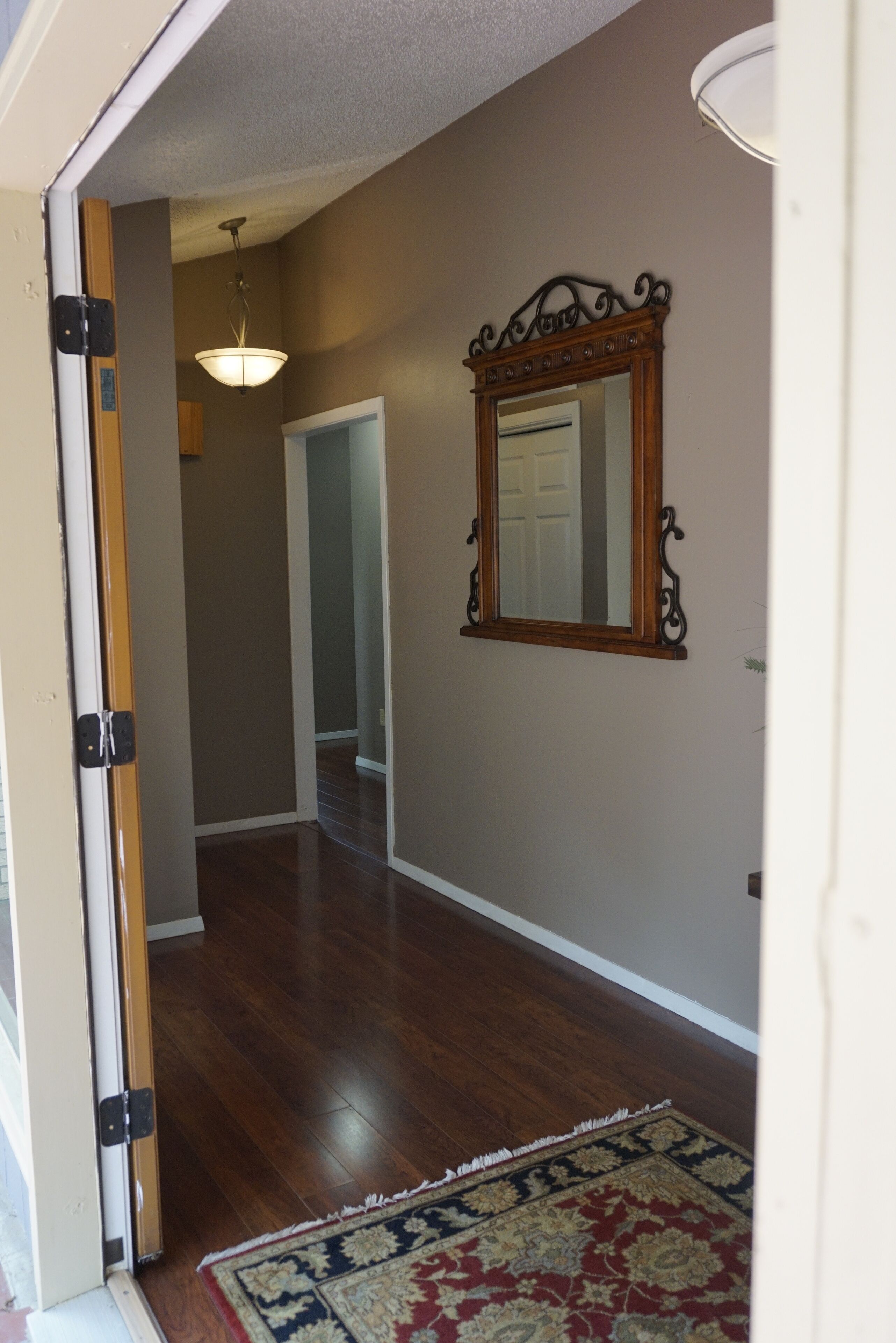 A hallway with wooden flooring, a patterned rug, and a decorative mirror on the wall.