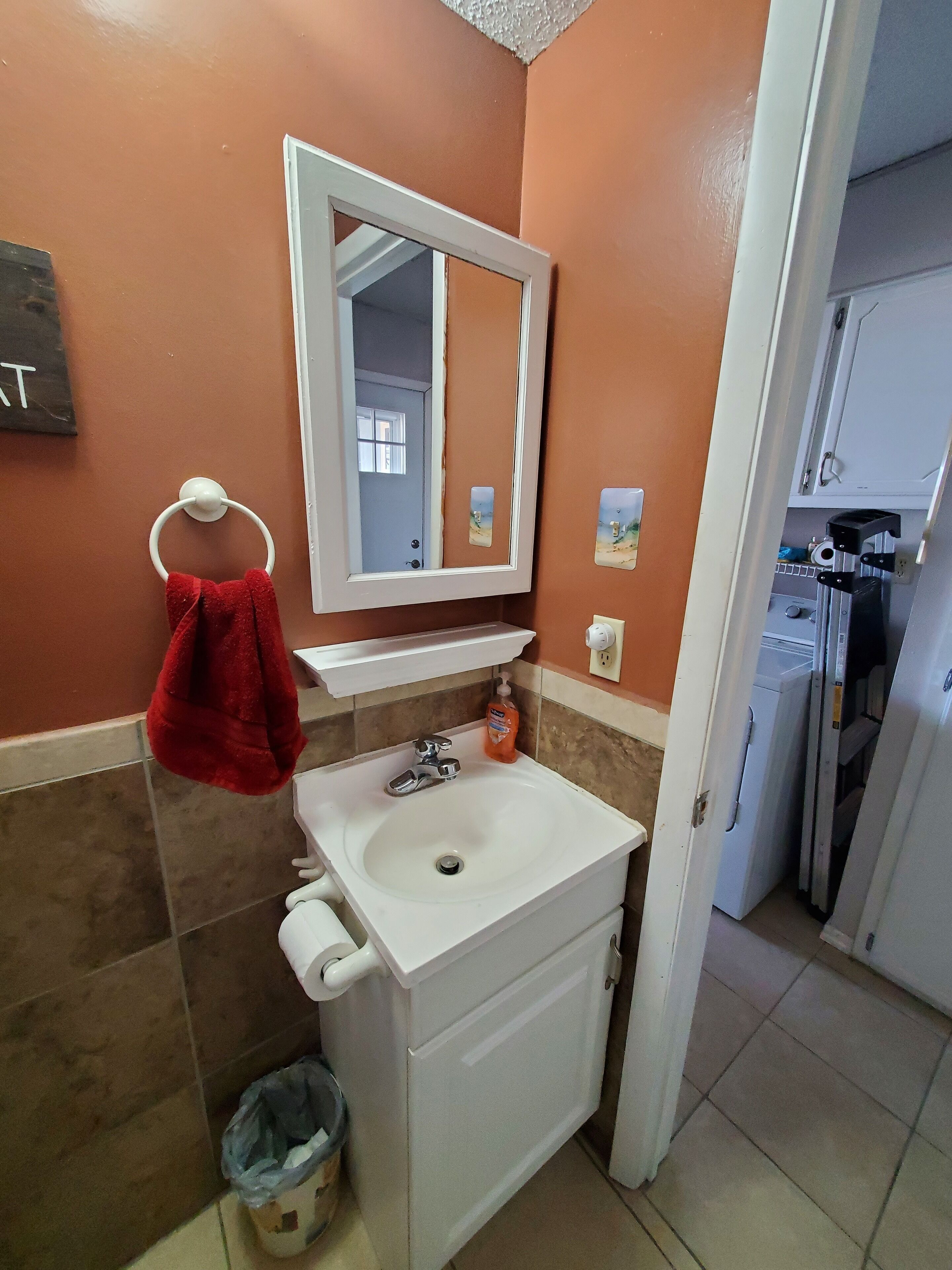 A bathroom with a white sink, a mirror, a red towel, and a trash bin.