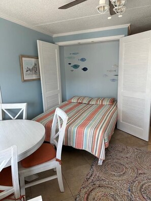 A room with a bed, a dining table with chairs, a ceiling fan, and a wall with fish decals.