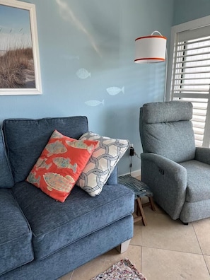 A living room with a blue sofa, a grey armchair, a small table, and a wall-mounted lamp.