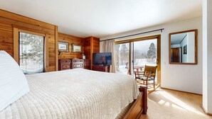 A bedroom with a large bed, wooden walls, a TV, a dresser, and a view of a snowy landscape through a sliding door. - Snowcreek III 448 Pet-Friendly, Spacious and Bright, Gorgeous Meadow Views by RedAwning (Mammoth Lakes)