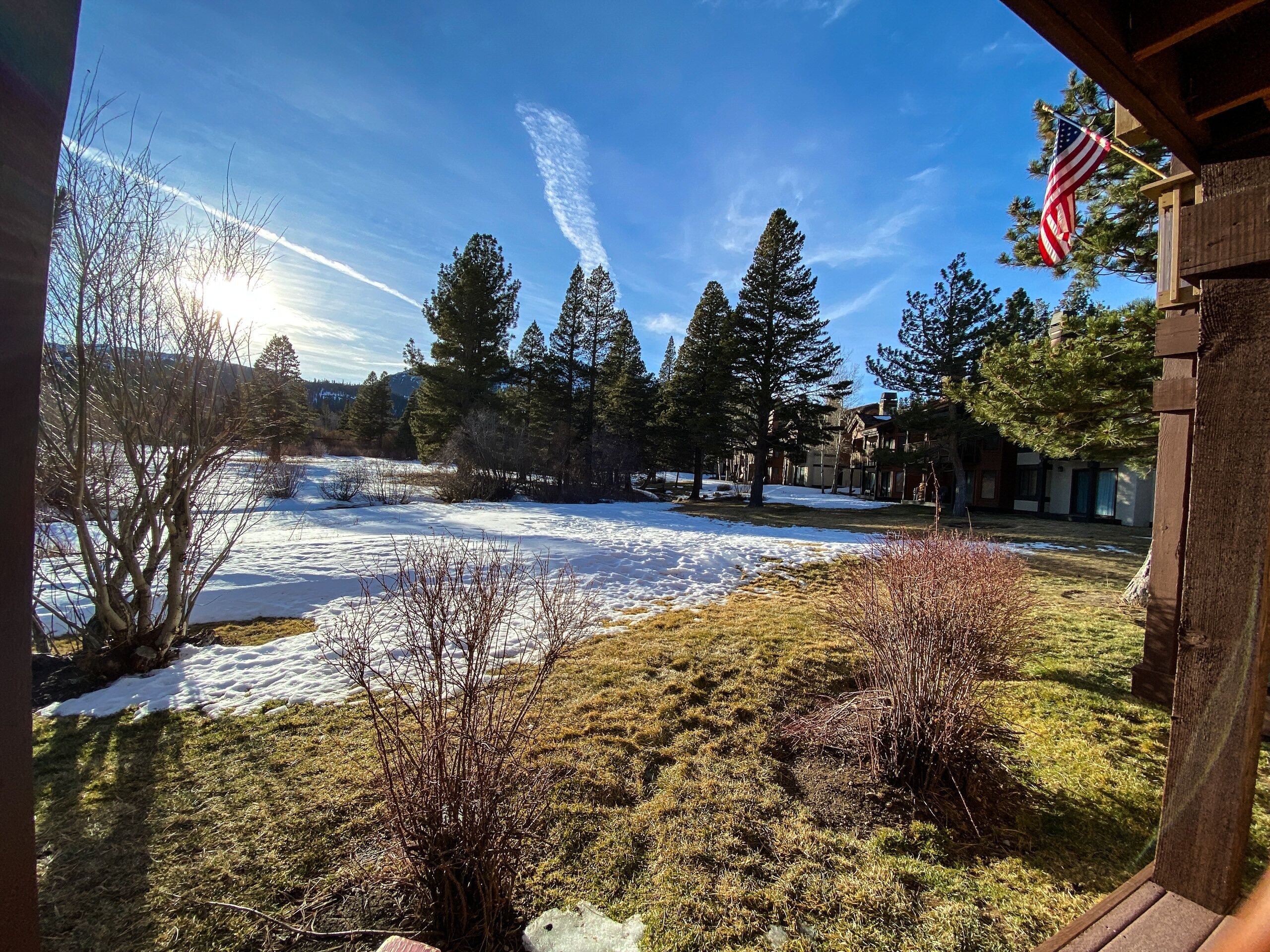 A snowy landscape with a clear sky, trees, and a wooden building with an American flag.