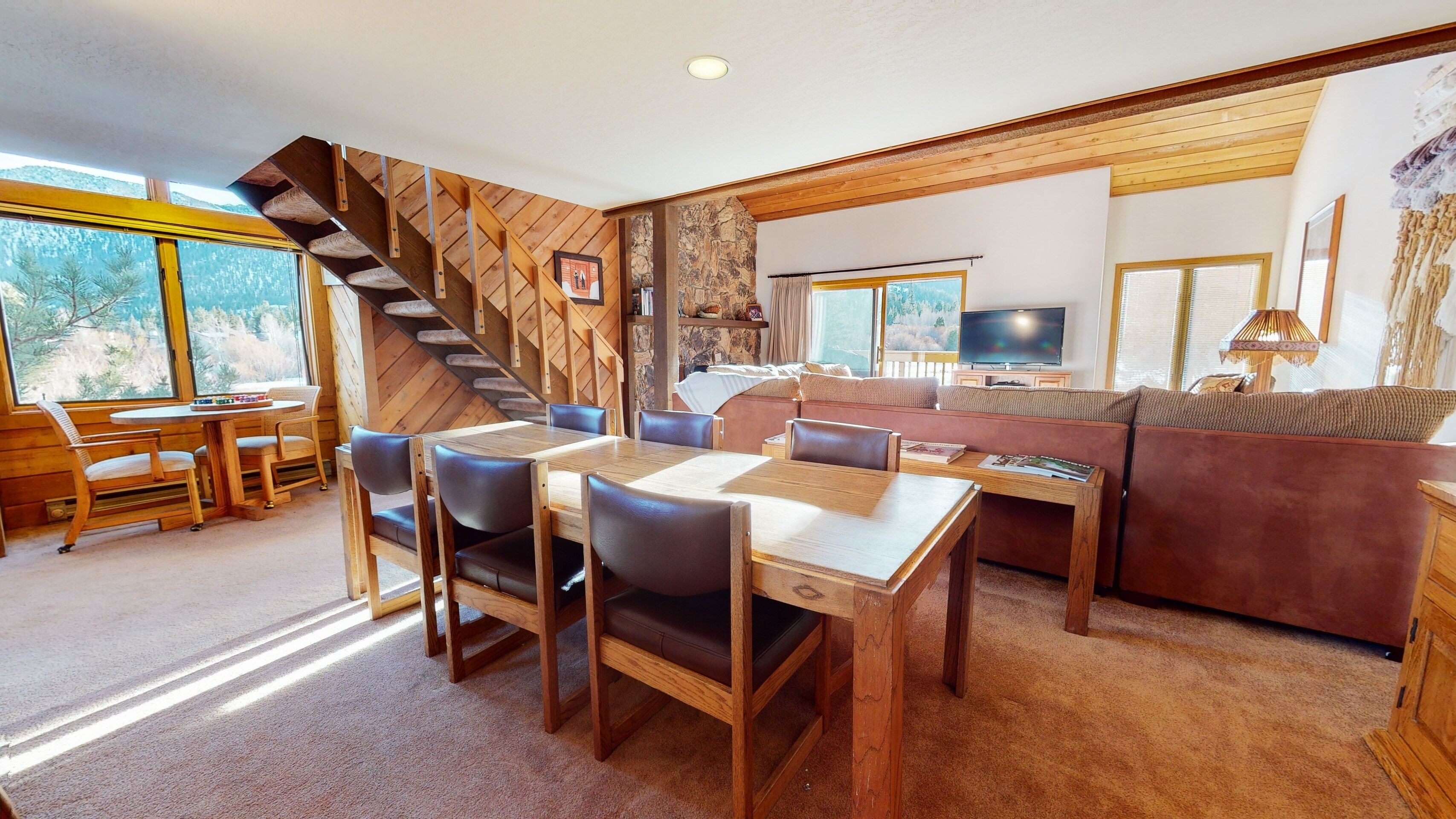 A cozy interior with a wooden dining table, chairs, a sofa, a TV, and a staircase.