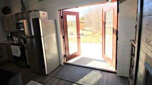 Une cuisine équipée d’un réfrigérateur en acier inoxydable, de meubles en bois et d’une porte-fenêtre coulissante donnant sur un jardin.