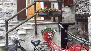 A stone building with a wooden staircase leading to a balcony. Two bicycles are parked in front, one with a basket and the other with a seat attached. - COTTAGE IN FORMER BARN WATERFALL VIEW (Piuro)