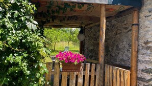 A rustic wooden gate with a hanging flower basket, a stone wall, and a wooden pergola with a patterned awning. - COTTAGE IN FORMER BARN WATERFALL VIEW (Piuro)