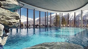 Piscina com águas cristalinas e azuis, rodeada por amplas janelas que oferecem vista para as montanhas.