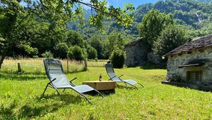 Two lounge chairs in a grassy area with a stone building in the background. - COTTAGE IN FORMER BARN WATERFALL VIEW (Piuro)