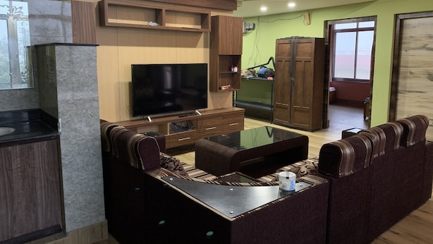 A modern living room with a flat-screen TV, a sofa, a coffee table, and built-in wooden cabinets. - 2BHK Apartment with Fast Internet (Siddharthanagar)
