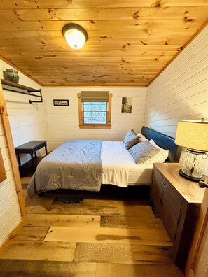A small, cozy room with a bed, a nightstand, a lamp, a window, and a sign that reads "BIKE DRINK".
