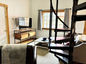 A compact living space with a TV on a wooden stand, a small table with a bowl, a sofa, and a bunk bed.