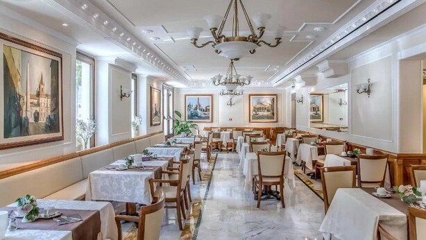 A spacious dining area with multiple tables and chairs, a chandelier, and framed cityscape paintings on the walls. - Alimandi Vaticano (Rome)