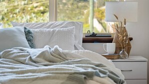 A bedroom with a bed, pillows, a bedside table with a lamp, a cup, and a vase with dried plants. - Beach Home: Epic Views: Private Enclosed Yard:Pets (Halls Head)