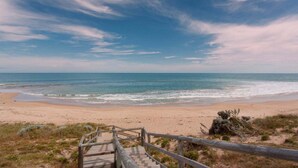 A beach with a wooden staircase leading down to the shore, surrounded by sparse vegetation. - Beach Home: Epic Views: Private Enclosed Yard:Pets (Halls Head)