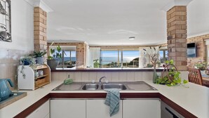 A modern kitchen with a large island, double sink, and a view of the ocean. - Beach Home: Epic Views: Private Enclosed Yard:Pets (Halls Head)