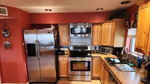 A modern kitchen with stainless steel appliances, wooden cabinets, and a patterned rug. - Beautiful Gated Retreat with Breathtaking Views of the Superstition Mountains (Apache Junction)