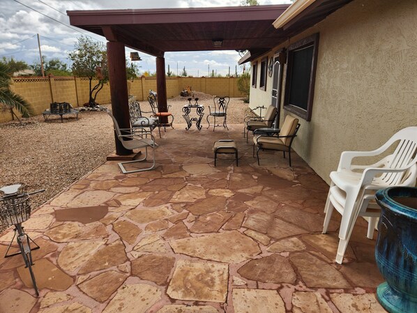Un patio con suelo de piedra, mobiliario exterior y una zona de estar cubierta.