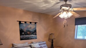 A bedroom with a bed, a nightstand, a lamp, a ceiling fan, a wall hanging, and a window. - Beautiful Gated Retreat with Breathtaking Views of the Superstition Mountains (Apache Junction)