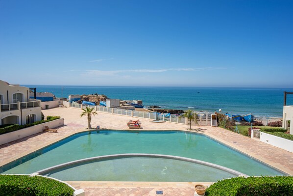 A pool area with a view of the ocean, a palm tree, and a boat.