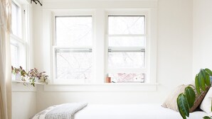 Ein Schlafzimmer mit einem Bett, zwei Fenstern, einer Pflanze und einem Teppich.