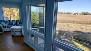 Une pièce dotée d’une grande fenêtre donnant sur un champ, d’une table ronde et d’un canapé à rayures bleues.