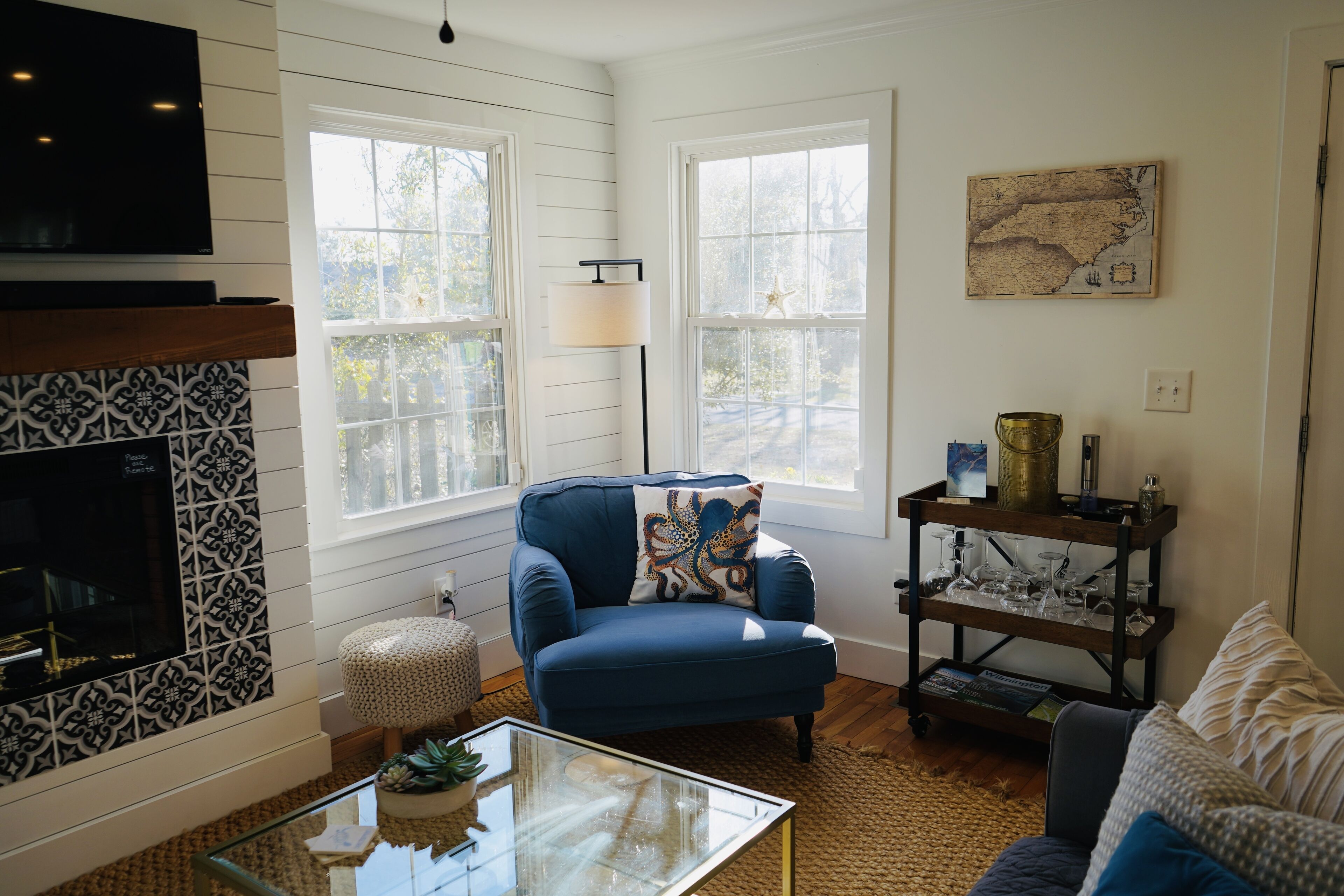 A living room with a blue armchair, a glass coffee table, a fireplace, and a bookshelf.
