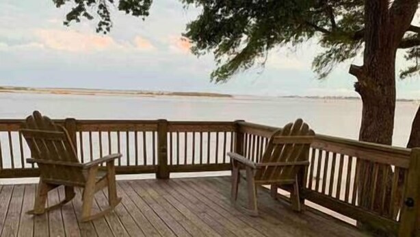 Een houten terras met twee Adirondack-stoelen gericht op een rustig waterlichaam.