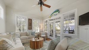 A spacious living room with a large sofa set, a wooden coffee table, and a ceiling fan. - Updated in Seaside, Amazing Porches, Close to West Side Pool + 2 Adult Bikes! (Santa Rosa Beach)