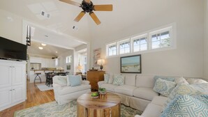 A spacious living room with a round coffee table, a white sofa, and a television. - Updated in Seaside, Amazing Porches, Close to West Side Pool + 2 Adult Bikes! (Santa Rosa Beach)