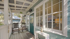 A covered porch with wooden chairs, a door, and a window with shutters. - Guest Home W/King in Seaside, FL 3 Min Walk to Beach, + 2 Adult Bikes! (Santa Rosa Beach)