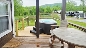 A wooden deck with a hot tub, a table, and chairs.