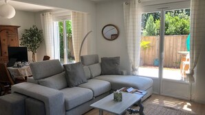 A living room with a grey sectional sofa, a small white table, and a large window with curtains. - CHARM AND TRANQUILITY ON THE ARCACHON BASIN (Andernos-les-Bains)