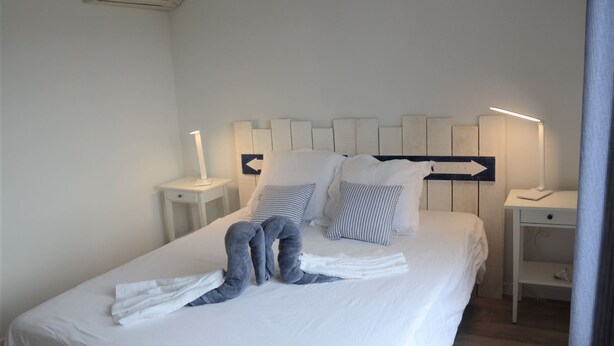 A neatly made bed with pillows, a bedside table with a lamp, and a wall-mounted air conditioner. - CHARM AND TRANQUILITY ON THE ARCACHON BASIN (Andernos-les-Bains)