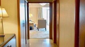 A hotel hallway with a wooden floor, a reception desk with a lamp, and a door leading to a room.